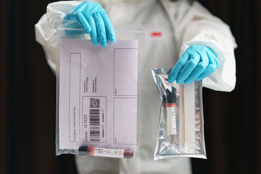 Coronavirus testing process, a hand holds tube of blood test samples and swab collection kit specimen sample testing. (FAKE QR codes/barcodes)