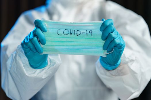 Scientist in hazmat suit, hand holding protective face mask with text covid-19.