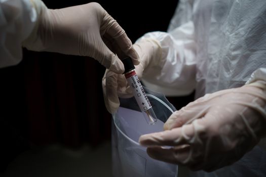 Doctor in a protective suit. taking blood test sample tubes with COVID-19 from a plastic zipper bag in laboratory. (swab ) (Fake QR code and barcode)