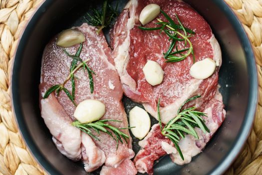 Raw beef steak and pork juicy steak with vegetables and spices in the pan.