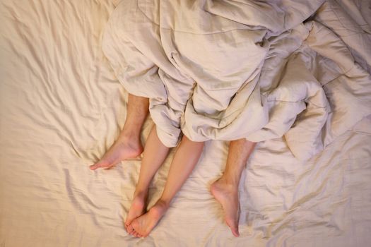 Close up of male and female feet on a bed having sex under sheets in the bedroom.