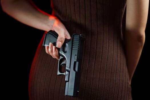 Woman hiding handgun behind her back on black background.