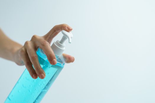 Hand with hand sanitizer in a clear pump bottle on a white background.