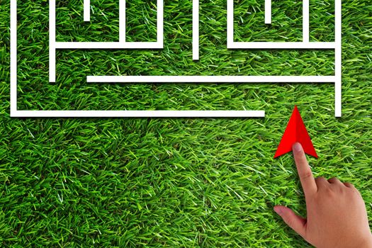 Business challenge, finding solution, resolve problem concept, hand holding red arrow and maze on green grass background