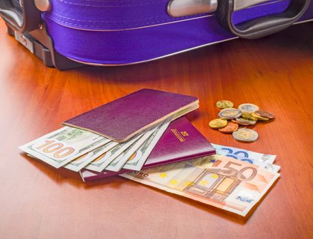 Dollars, Euros and Passports with a violet suitcase, ready for a business or holiday travel abroad.