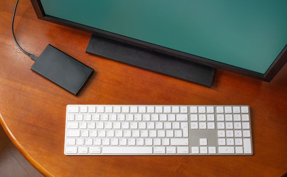 A computer monitor, a digital wireless keyboard and a hard disk drive on a round wooden desk