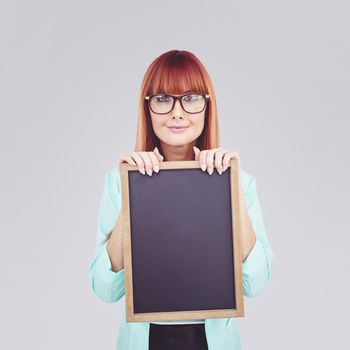 Smiling hipster woman holding blackboard against light grey