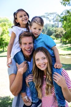 Happy parents carrying their kids on the shoulder in the park on a sunny day