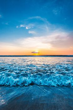 Sea waves at sandy beach at sunset, sun hiding behind a cloud