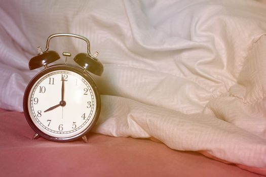Black alarm clock on the bed with sunrise, wake up concept, vintage and retro style