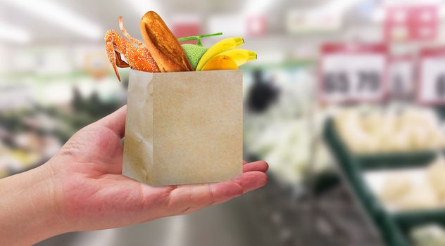 Grocery shopping concept, hand holding supermarket retail product in brown paper bag on blur background