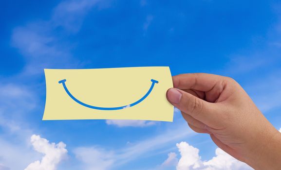 Happiness concept, hand and paper smile on blue sky background