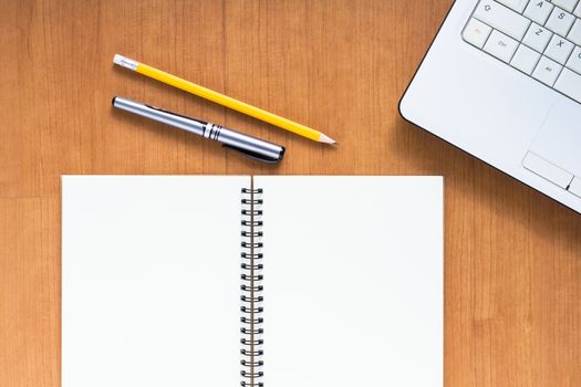 Blank notebook and computer with pen and pencil on wood table, business concept
