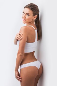 Young beautiful woman in white cotton underwear touching own skin standing , white background
