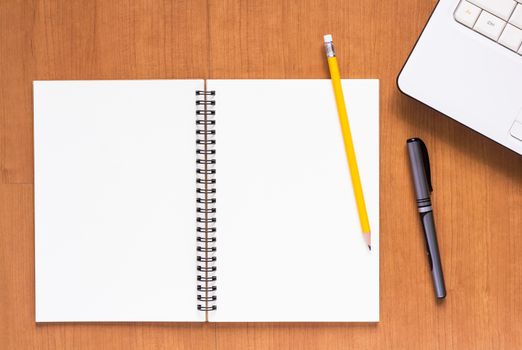 Blank notebook and computer with pen and pencil on wood table, business concept