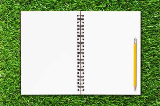 Blank notebook and yellow pencil on green grass background, ecology and nature concept