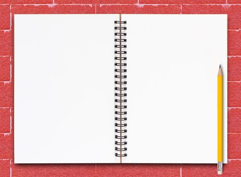 Open notebook and yellow pencil on red brick background