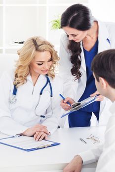 Female doctor , her assistant and patient filling forms in medical clinic office