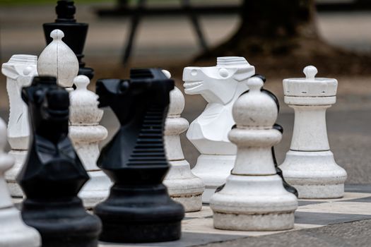 Outdoor chess board with big plastic pieces. Outdoor giant chess in public area zone, Close up big pieces of street chess in the park - image