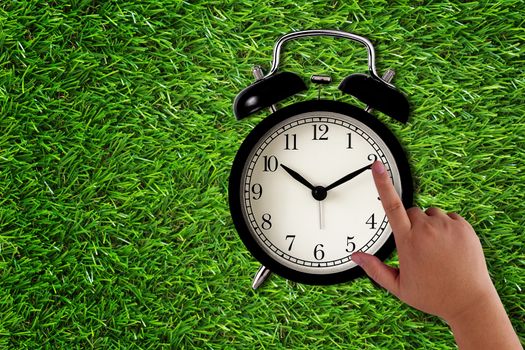 Time management concept, business planning, hand holding alarm clock on green grass background
