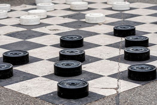 Large plastic checkers painted on the pavement cells in a city park - image