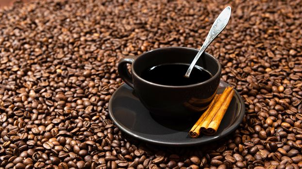 Black coffee mug and cinnamon sticks on the coffee beans background - image