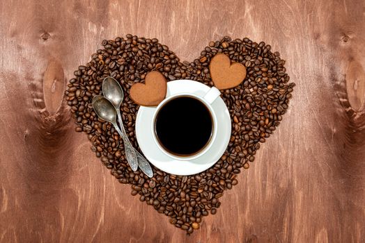 White coffee mug, heart shaped gingerbread and two spoons on a heart shaped base made from coffee beans - image