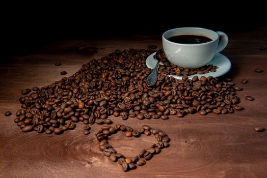 White coffee mug and coffee beans on the dark wooden background, Heart shape from coffee beans in the foreground - image