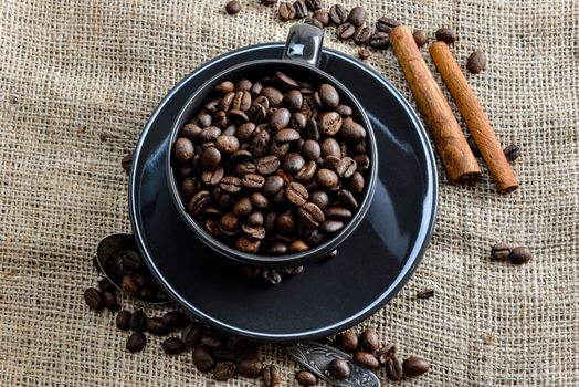 Black coffee mug full of organic coffee beans and  cinnamon sticks on linen cloth - image