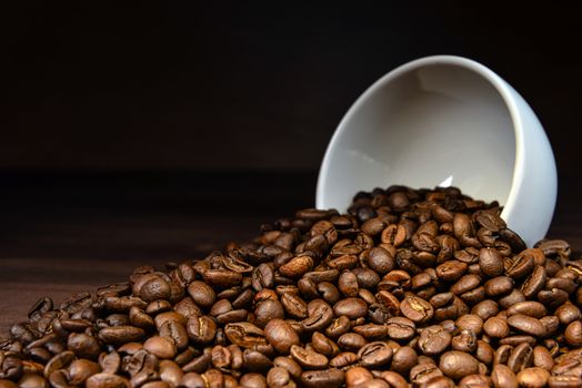 Coffee bean pouring out of a white mug on wooden table - image