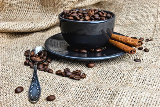 Black coffee mug full of organic coffee beans and  cinnamon sticks on linen cloth - image