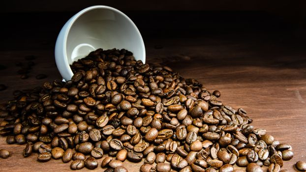 Coffee bean pouring out of a white mug on wooden table - image