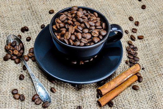 Black coffee mug full of organic coffee beans and  cinnamon sticks on linen cloth - image