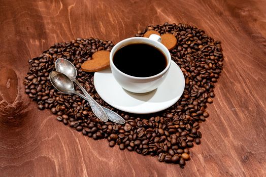 White coffee mug, heart shaped gingerbread and two spoons on a heart shaped base made from coffee beans - image