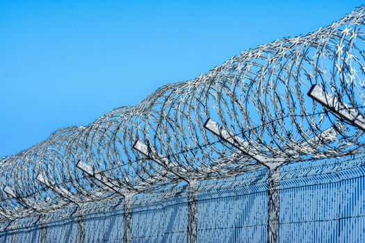fence with barbed wire against blue sky with clouds, security concept