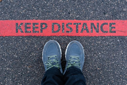 man in sneakers standing next to a red line with text KEEP DISTANCE, restriction or safety warning concept