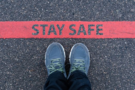man in sneakers standing next to a red line with text STAY SAFE, restriction or safety warning concept