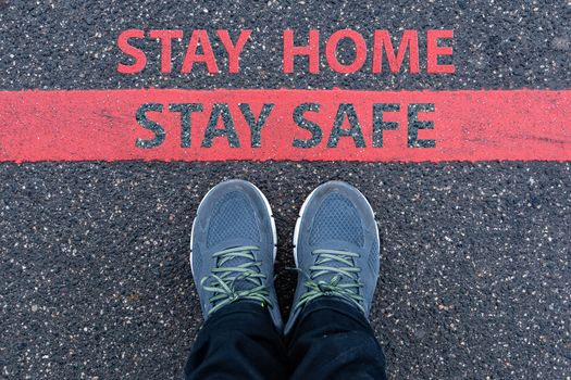 man in sneakers standing next to a red line with text STAY HOME, STAY SAFE, restriction or safety warning concept