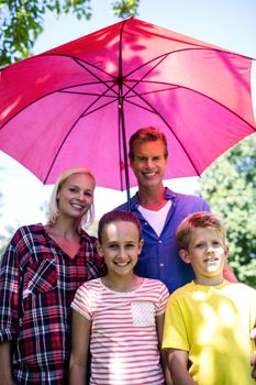 Portrait of family standing under pink umbrella in park