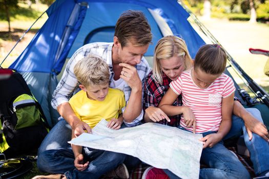 Family sitting in front of tent and looking at map in park