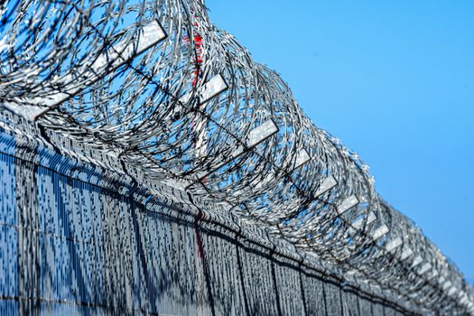 fence with barbed wire against blue sky with clouds, security concept