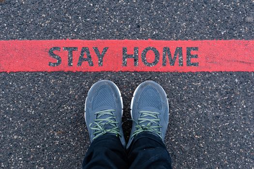 man in sneakers standing next to a red line with text STAY HOME, restriction or safety warning concept