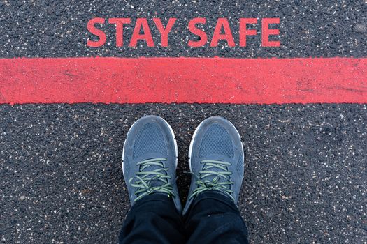 man in sneakers standing next to a red line with text STAY SAFE, restriction or safety warning concept