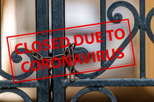 Closed Due To Coronavirus - sign on the background of an ornamental iron gate locked with chain