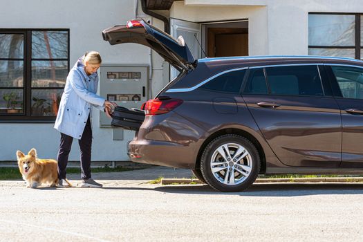 woman with dog loading suitcase into car trunk, preparation for trip