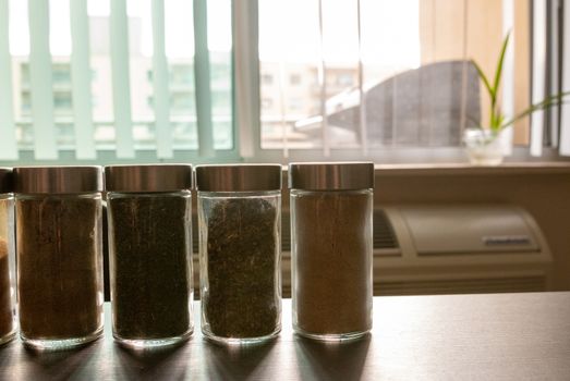 Assortments of spices, white pepper, chili flakes, lemongrass, coriander and cumin seeds in jars on grey stone background