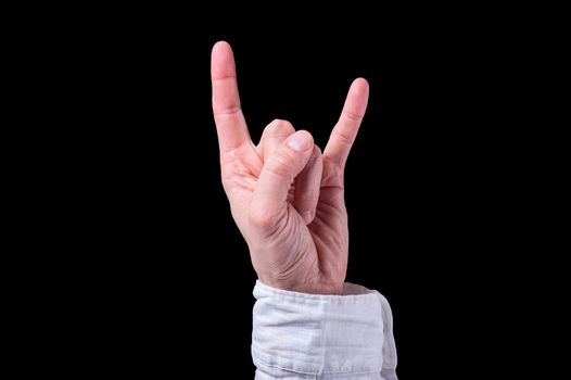 Human hand in a white shirt shows The sign of the horns on isolated black background