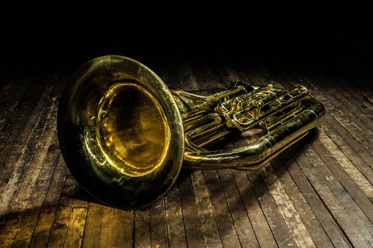 golden brass wind instrument euphonium lies on a brown wooden stage in the light of a spotlight