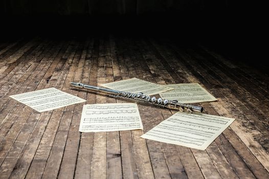 flute lies on a wooden stage among sheet music with notes