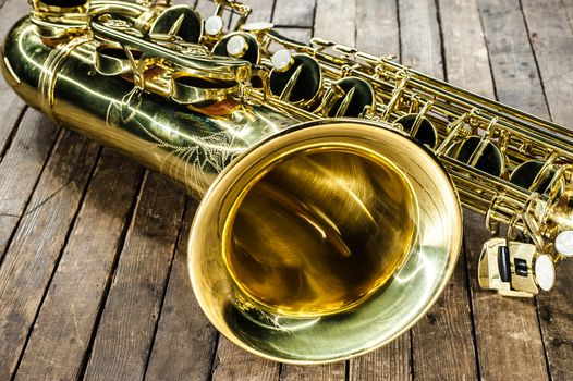 piece of yellow saxophone - bell and valves on a vintage wooden surface